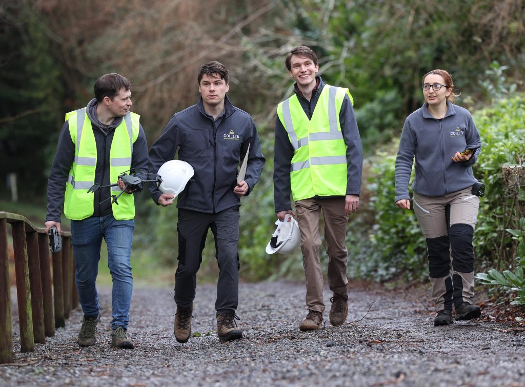 Four members of Coillte walking in a forest with high-vis vests and hard hats.
