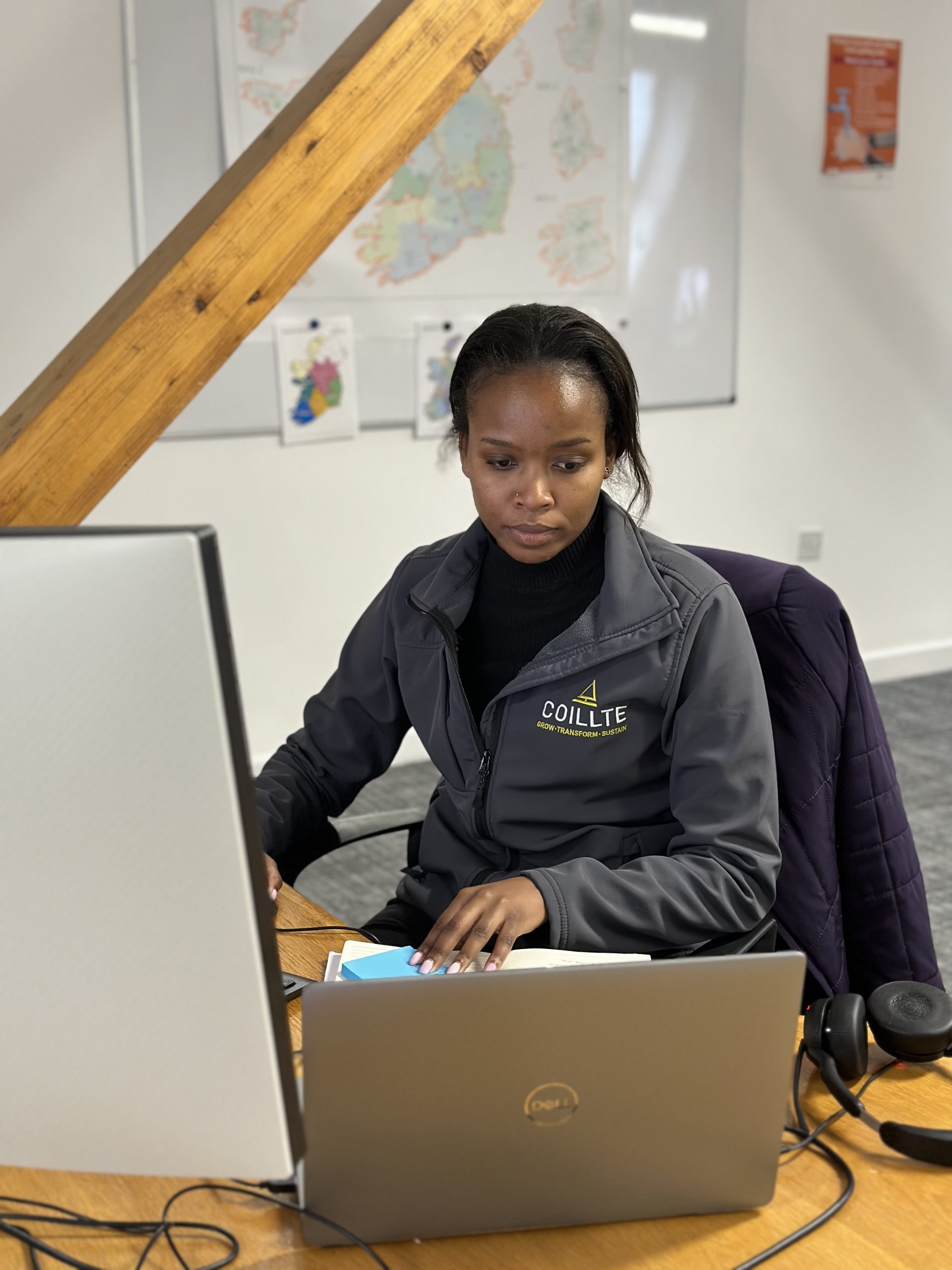 Sharon Njoya Picture of Coillte Graduate, Sharon, working in an office at a laptop and desktop computer