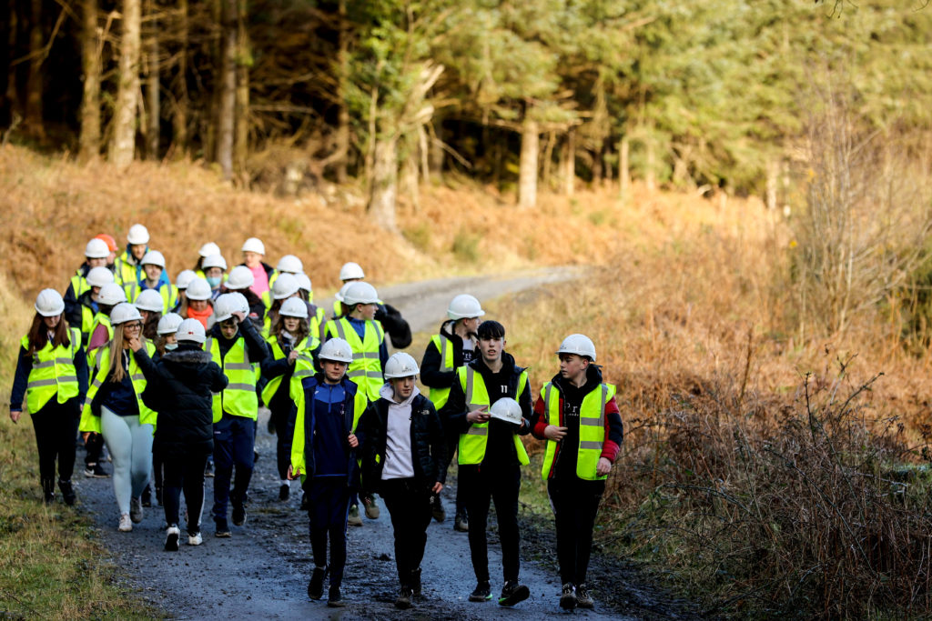 Large group of students walking a sunny forest road all wearing high visibility jackets