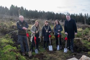 Representatives of the five dublin mountains partner organisations satnding in a forest with shovels carrying red ribbons getting ready to plant a tree each