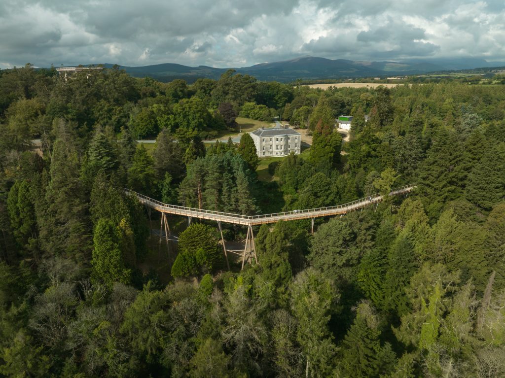 Drone shot of wooden treetop walk stretching across the forest canopy with Avondale House in the background