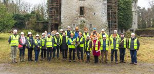 Group of people in high vis vests and hard hats standing in front of a castle being restored