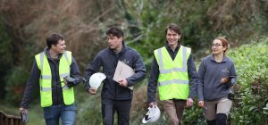 Four forsters, walking along a forest road carrying hard hats and forestry equipment