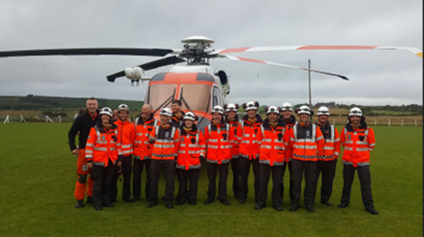 Picture of Irish Coast guard team in red high visibility jackets standing in front of the rescue helicopter which is parked on a football pitch