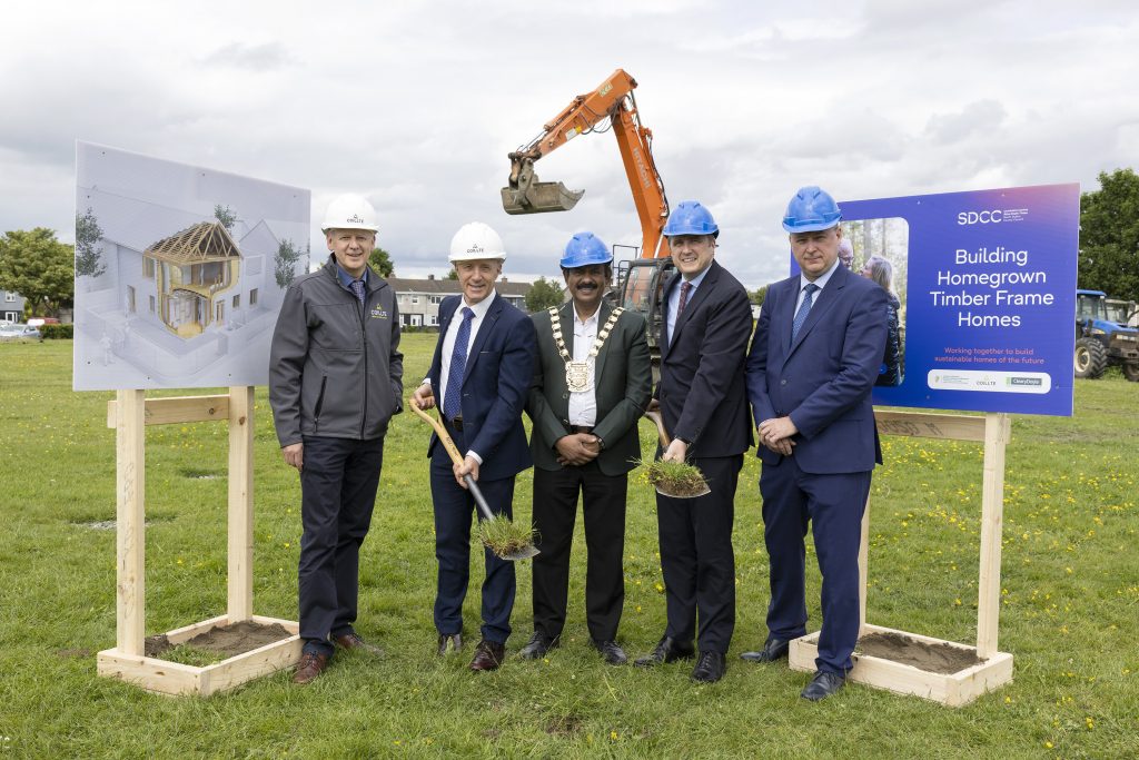 five men wearing suts and hard hats with shovels posing in front of a sign and a digging machine for a project launch
